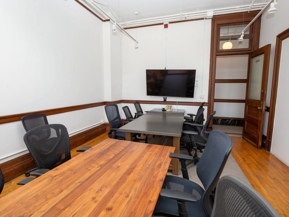 Two long tables with office chairs near a TV and open door.