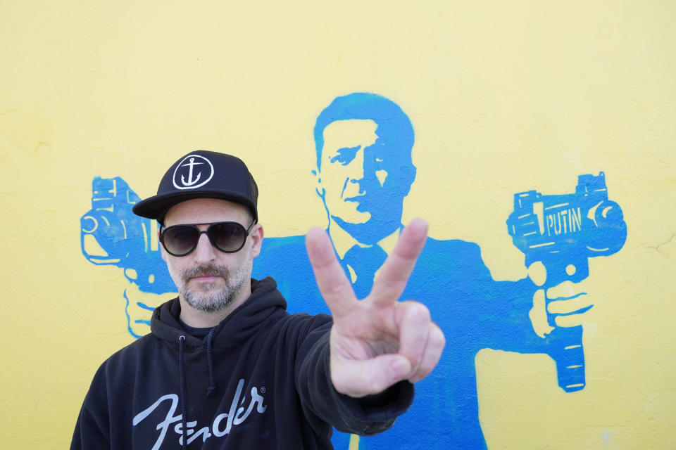 Street artist Todd Goodman, known as 1GoodHombre, stands in front of his stencil of Ukrainian President Volodymyr Zelenskyy holding submachine guns, painted without a permit on a building's wall in Santa Monica, Calif., on Monday, March 21, 2022. Goodman came out of anonymity as a street artist, risking arrest and fines for his unlicensed work to solicit funds for Ukrainian war refugees. (AP Photo/Eugene Garcia)