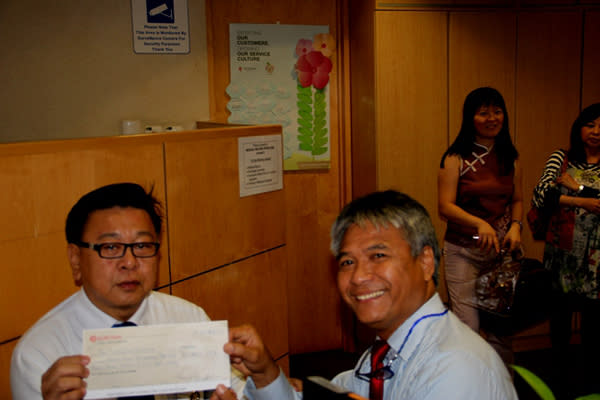 Club President Budi Soehardi and treasurer Chris Pan signing the cheque to clear Nitcharee's hospital bills. (Photo courtesy of Rotary E-club of Singapore)