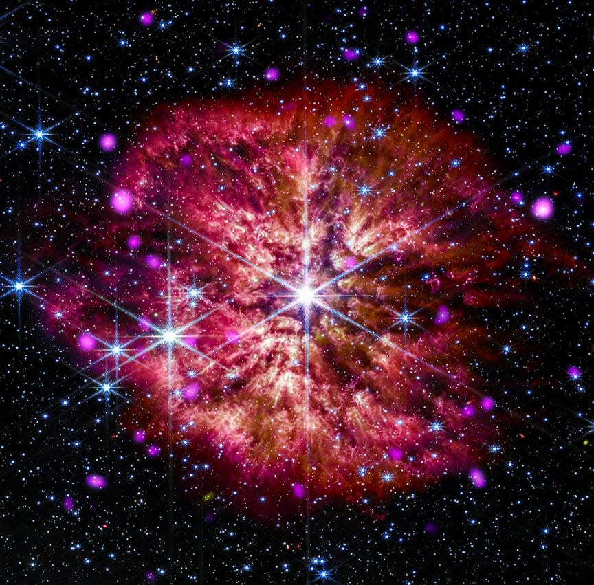 bright star with diffraction spikes cutting through a red billowing cloud in space surrounded by smaller purple stars