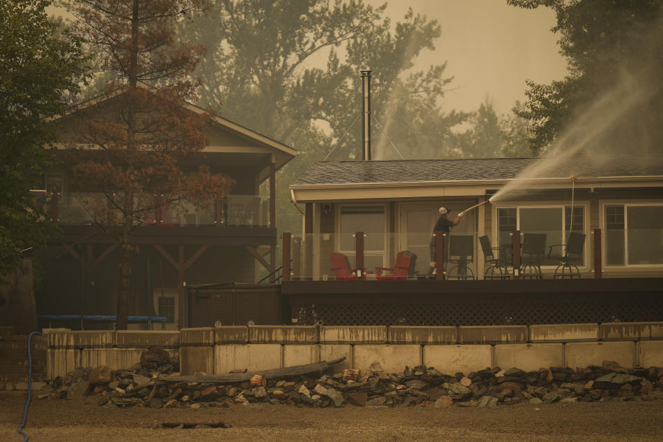 Trevor Manzuik, quien fue evacuado de su vivienda debido a un incendio forestal, rocía su propiedad luego de regresar a casa en bote, el domingo 20 de agosto de 2023, en la Columbia Británica, Canadá. (Darryl Dyck/The Canadian Press vía AP)