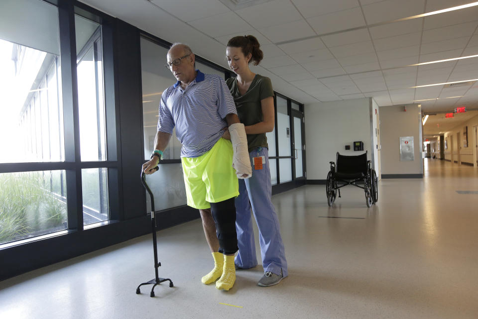 FILE - In this Aug. 28, 2018 file photo, shark attack victim William Lytton, of Scarsdale, N.Y. is assisted by physical therapist Caitlin Geary at Boston's Spaulding Rehabilitation Hospital. Lytton suffered deep puncture wounds to his leg and torso after being attacked by a shark on Aug. 15, 2018 while swimming off a beach in Truro, Mass. A prominent shark researcher says smaller, younger great white sharks are being spotted in greater numbers off Cape Cod. (AP Photo/Steven Senne, File)