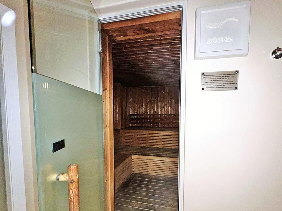 An open glass door revealing a sauna with a white sign saying "sauna" next to the door
