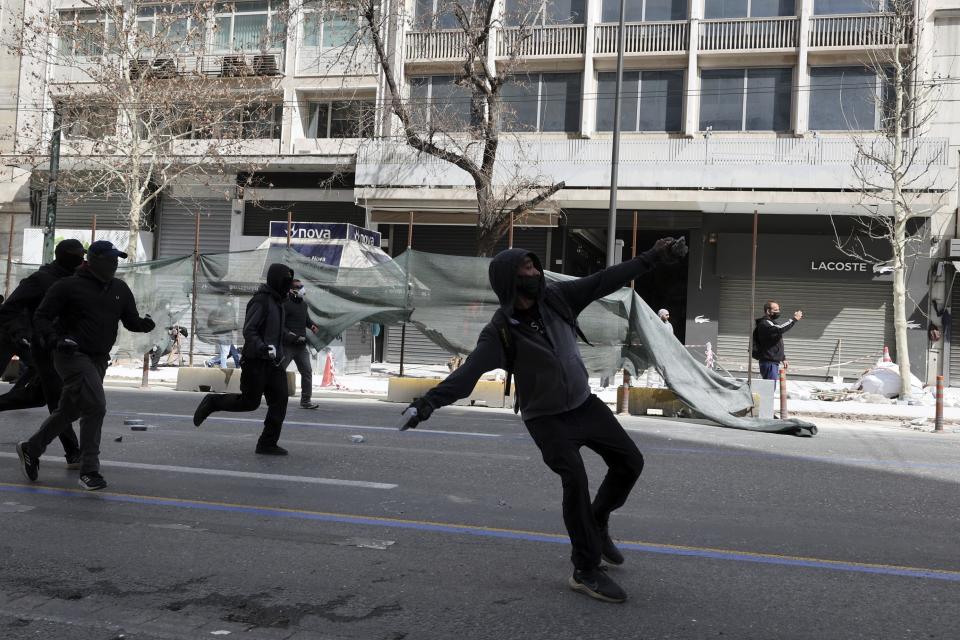Hooded demonstrators throw stones against riot police during clashes in Athens, Greece, Sunday, March 5, 2023. Thousands protesters, take part in rallies around the country for fifth day, protesting the conditions that led the deaths of dozens of people late Tuesday, in Greece's worst recorded rail accident. (AP Photo/Yorgos Karahalis)