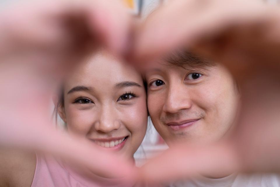 A couple in love makes heart-shaped hand gesture. (Photo: Getty Images)