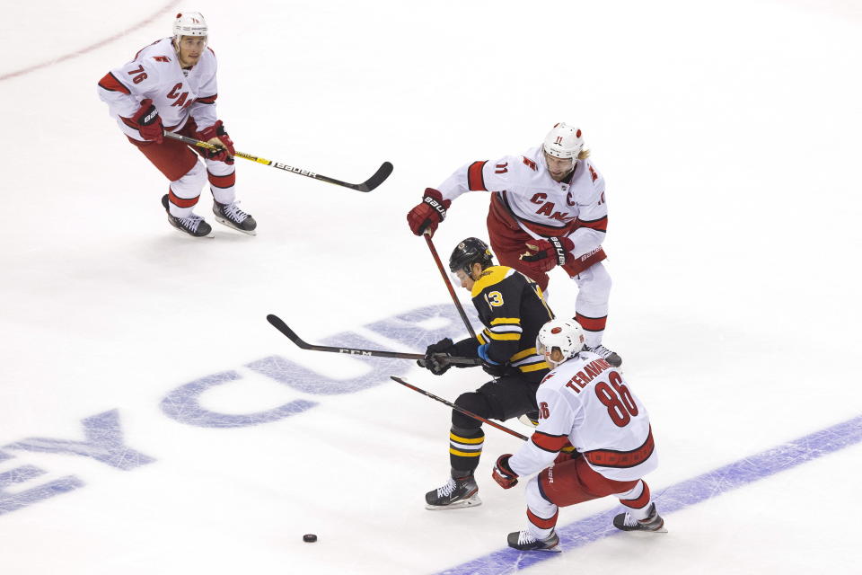 Boston Bruins' Charlie Coyle (13) moves the puck between Carolina Hurricanes' Teuvo Teravainen (86) and Jordan Staal (11) as Hurricanes' Brady Skjei (76) looks on during the third period of an NHL Eastern Conference Stanley Cup hockey playoff game in Toronto, Thursday, Aug. 13, 2020. (Chris Young/The Canadian Press via AP)