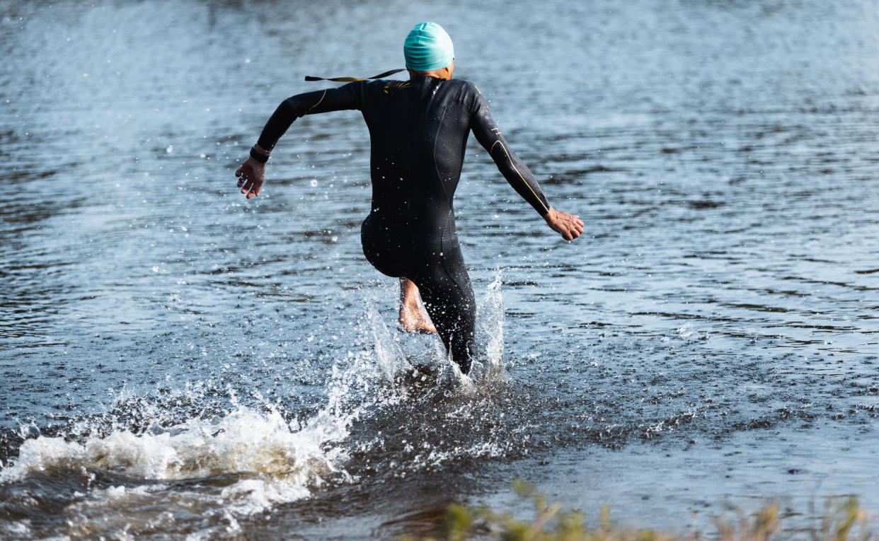 Professional triathlete swimming in river's open water. Man wearing swim equipment practicing triathlon on the beach in summer's day. Concept of healthy lifestyle, sport, action, motion and movement.