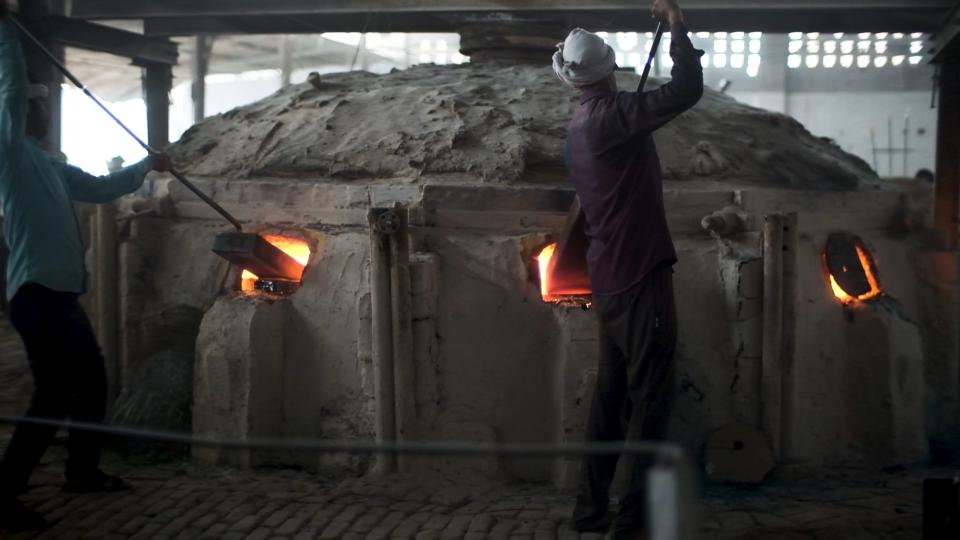 Workers dump sand and glass into a furnace