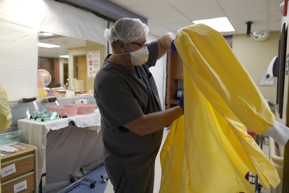 FILE - In this Nov. 24, 2020, file photo, Dr. Shane Wilson puts on personal protective equipment before performing rounds in a portion of Scotland County Hospital set up to isolate and treat COVID-19 patients in Memphis, Mo. Amid the coronavirus resurgence, states have begun reopening field hospitals to handle an influx of sick patients that is pushing health care systems — and their workers — to the breaking point. Hospitals are bringing in mobile morgues. And funerals are once again being livestreamed or performed as drive-by affairs. (AP Photo/Jeff Roberson, File)