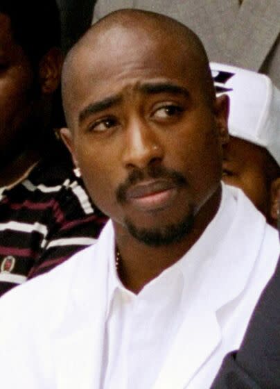 An old photo of Tupac Shakur wearing a white suit and looking to his left.