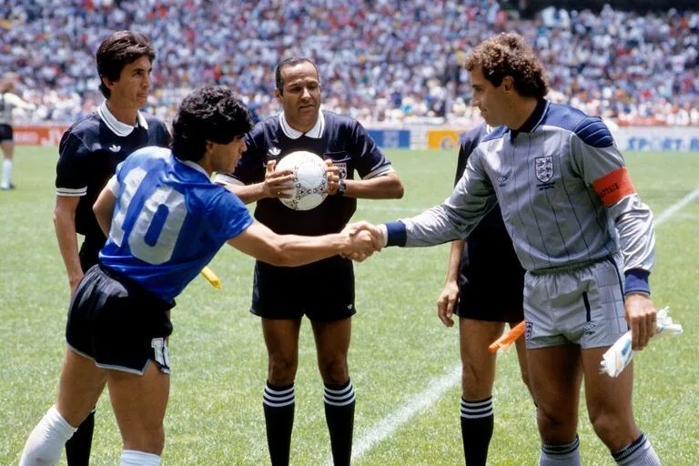 Diego Maradona saluda a Peter Shilton mientras el árbitro Ali Bennaceur (Ali Bin Nasser) controla la pelota.