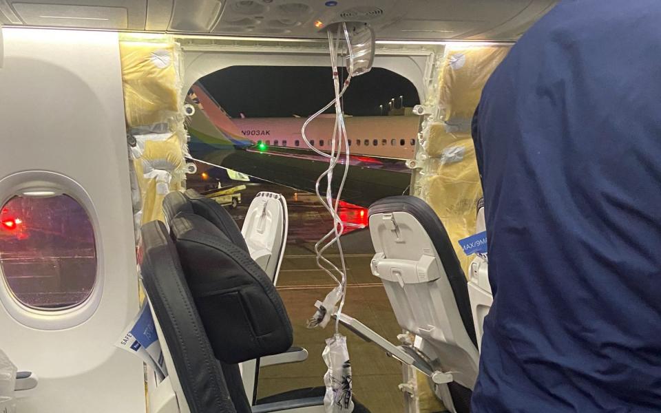 Passenger oxygen masks hang from the roof next to a missing window and part of a sidewall of an Alaska Airlines Flight 1282