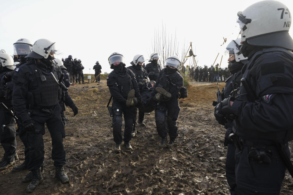 Police officers carry away a demonstrator to clear a road at the village Luetzerath near Erkelenz, Germany, Tuesday, Jan. 10, 2023. The village of Luetzerath is occupied by climate activists fighting against the demolishing of the village to expand the Garzweiler lignite coal mine near the Dutch border. Poster read: „1,5 degrees celsius means: Luetzerath stays". (AP Photo/Michael Probst)