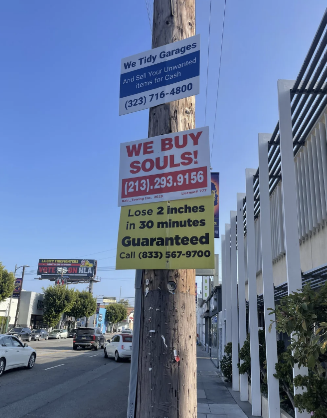 Multiple humorous signs on a pole offering services such as "We Buy Souls" and "Lose 2 inches in 30 minutes, Guaranteed."