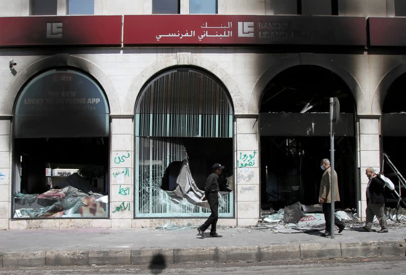 FILE PHOTO: People walk past burned-out bank facade that was set ablaze during unrest overnight in Tripoli