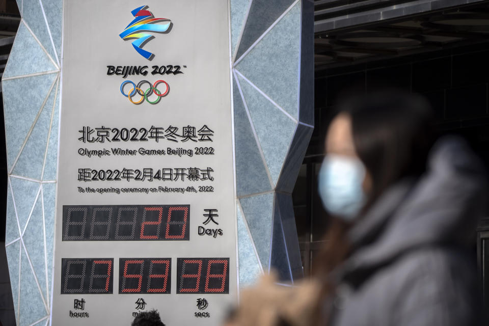 FILE - A woman wearing a face mask to protect against COVID-19 walks past a clock counting down the time until the opening ceremony of the 2022 Winter Olympics in Beijing, Saturday, Jan. 15, 2022. Beijing has reported its first local omicron infection, according to state media, weeks before the Olympic Winter Games is due to start. (AP Photo/Mark Schiefelbein, File)
