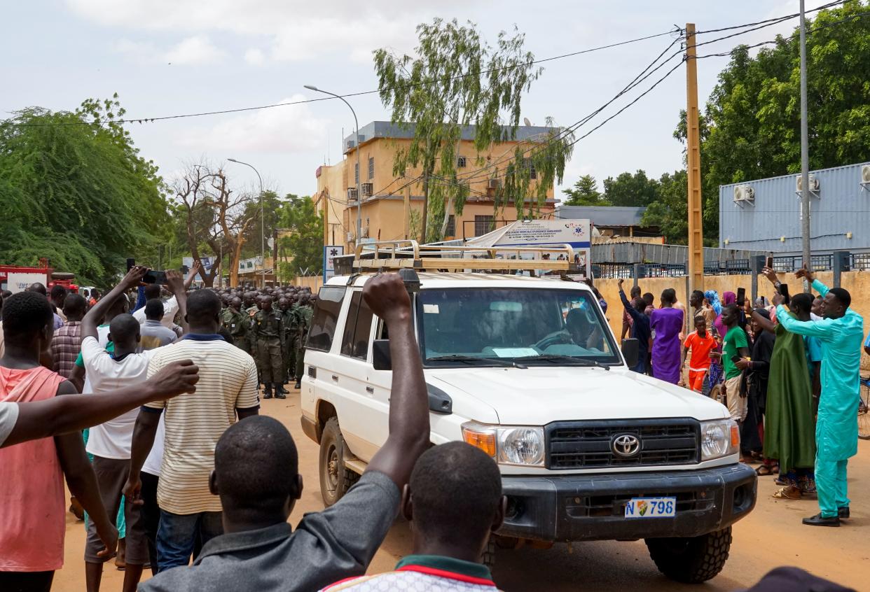 A vehicle drives through a crowd in Niamey as protesters cheer for security forces.