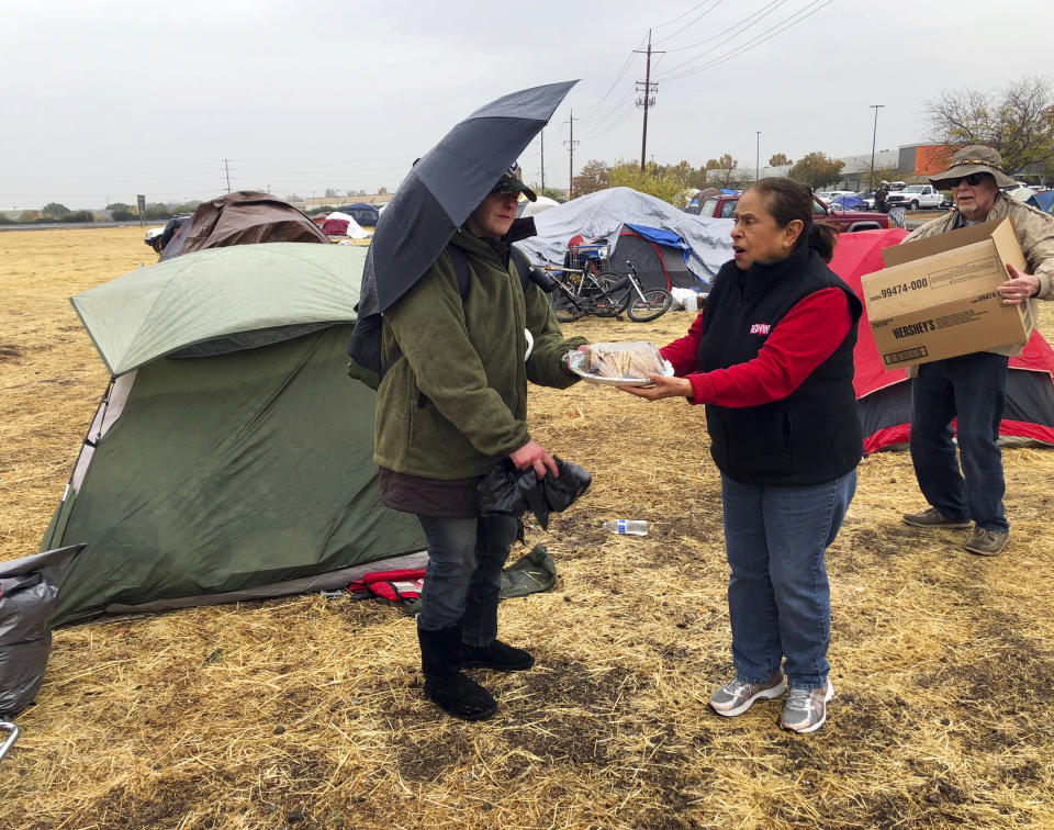 FILE - In this Nov. 21, 2018, file photo, Amy Sheppard accepts banana bread from Margarita and William Bradbury as she packs up items outside her tent in a Walmart parking lot in Chico, Calif., that's been a makeshift campground for people displaced by wildfire. Sheppard lost her home in Magalia to the Camp fire. Authorities are lifting evacuation orders for some Northern California communities ravaged by the state’s deadliest wildfire but said no traffic will be allowed into the town of Paradise. The Butte County Sheriff's office on Sunday, Dec. 2, said residents of neighborhoods in nearby Magalia can return to the area at noon on Sunday and public access would resume 24 hours later. (AP Photo/Kathleen Ronayne, File)