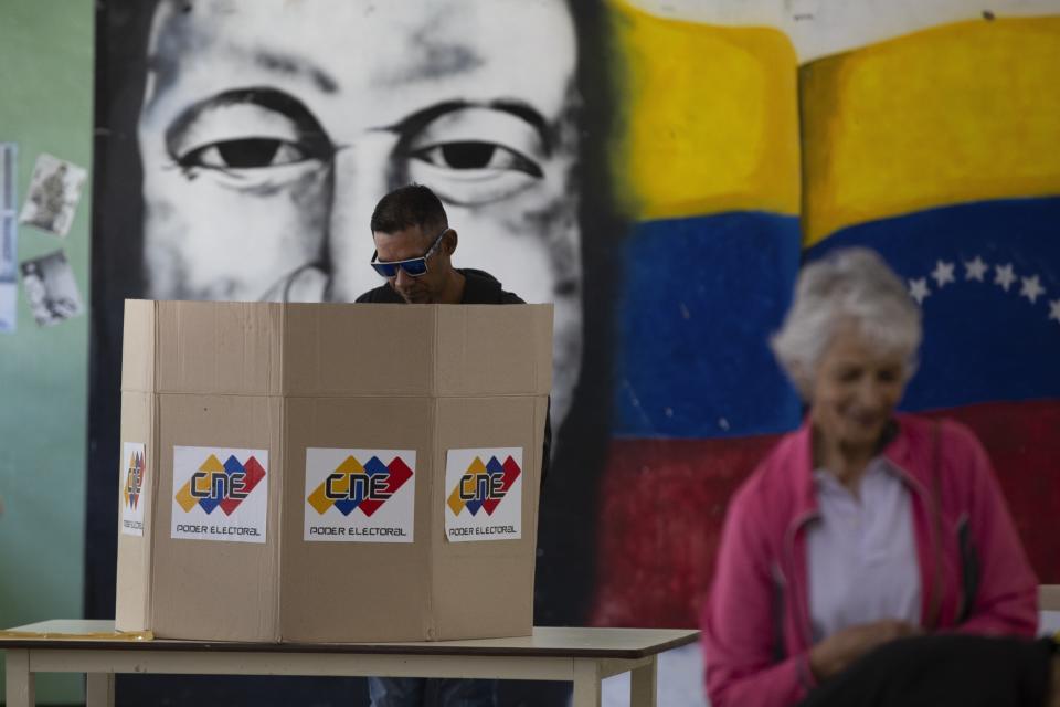Un hombre deposita su voto frente a un mural del fallecido presidente Hugo Chávez como parte de un ensayo para las elecciones presidenciales del 28 de julio en un centro de votación en Caracas, Venezuela, el domingo 30 de junio de 2024. (Foto AP/Cristian Hernández Fortune)