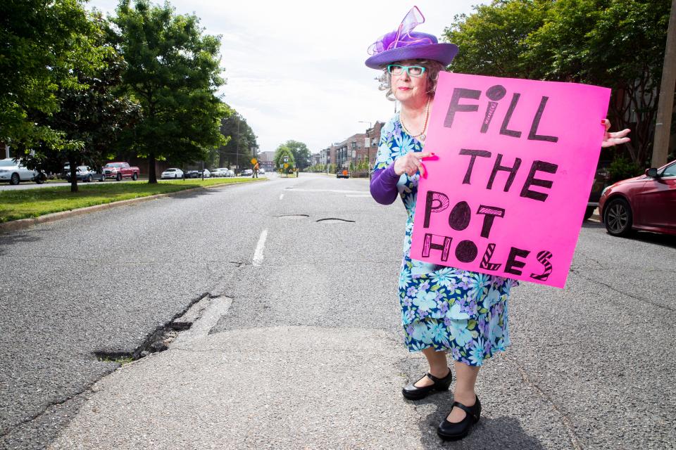 Sybil Presley, known as “The Pothole Lady,” poses for a portrait next to multiple potholes on Jefferson Avenue while holding a sign she made in Memphis, Tenn., on Friday, April 26, 2024. Presley appeared as this character at a recent Memphis City Council meeting and sang an original song, “The Pothole Blues.”