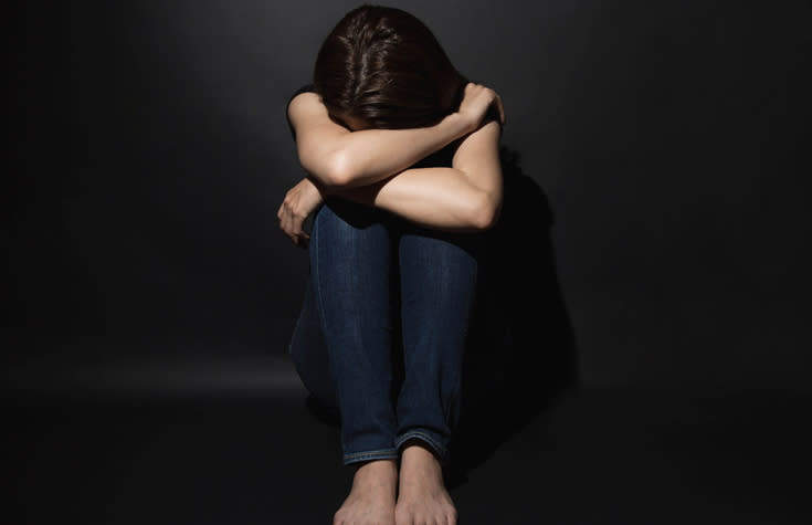 A depressed young woman is pictured with her head in her hands sitting alone.