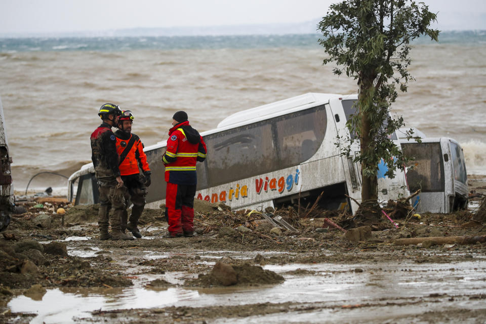 Rescuers stand next to a bus carried away after heavy rainfall triggered landslides that collapsed buildings and left people missing, in Casamicciola, on the southern Italian island of Ischia, Italy, Saturday, Nov. 26, 2022. (AP Photo/Salvatore Laporta)