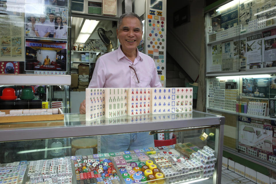 In this April 18, 2019, photo, Cheung Shun-king, 65-year-old mahjong game tiles maker, poses with his mahjong tiles in his decades-old store 100 square feet downstairs shop in a Kowloon's old neighborhood of Hong Kong. Hand-carved mahjong tiles is a dying art in Hong Kong. But Cheung is trying to revive the heritage/raise people's interest by organizing hand-craved tile class to keep the tradition alive. (AP Photo/Kin Cheung)