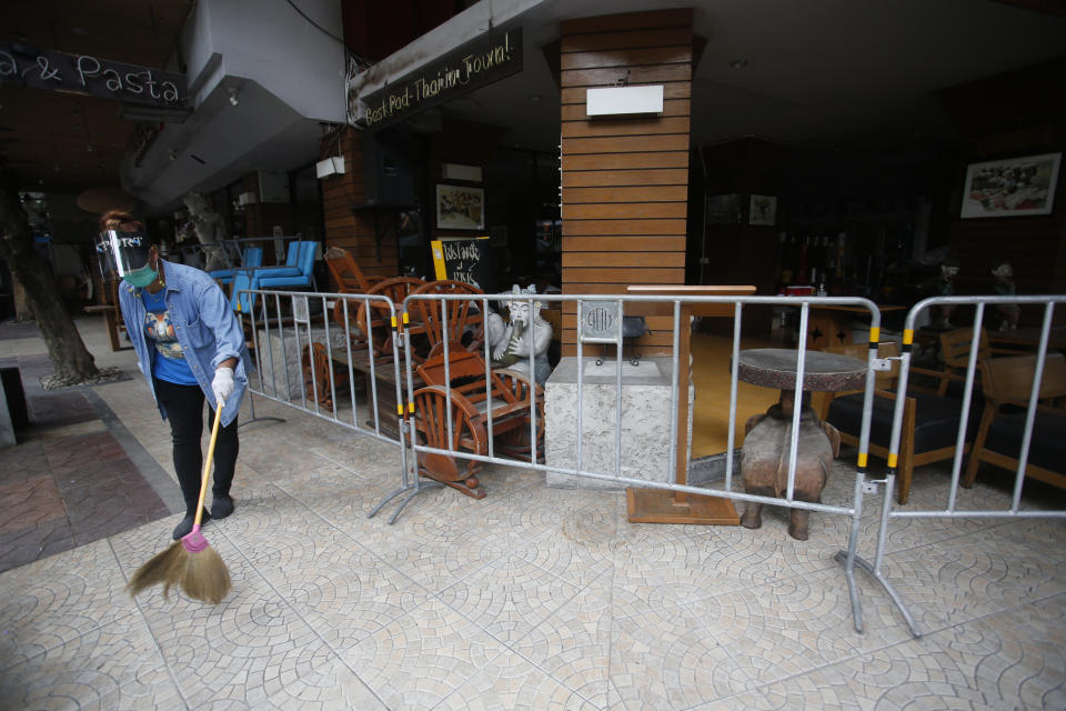 A worker wearing a face mask to help curb the spread of the coronavirus sweeps with a broom around a restaurant in Khao San road, a popular hangout for Thais and tourists in Bangkok, Thailand, Monday, April 26, 2021. Cinemas, parks and gyms were among venues closed in Bangkok as Thailand sees its worst surge of the pandemic. A shortage of hospital beds, along with a failure to secure adequate coronavirus vaccine supplies, have pushed the government into imposing the new restrictions. (AP Photo/Anuthep Cheysakron)