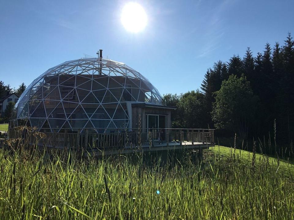 dome-shaped norway earthship under blue sky in a field