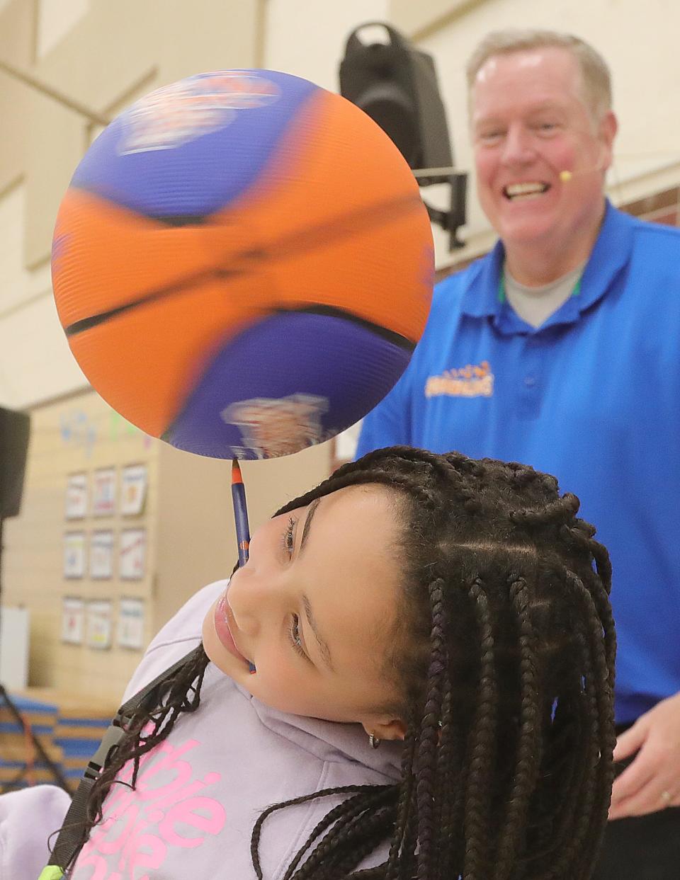 McKenzie Beverly-White holds a pen in her mouth to balance a spinning basketball during a performance with Jim "Basketball" Jones at Herberich Primary School on Tuesday in Fairlawn.