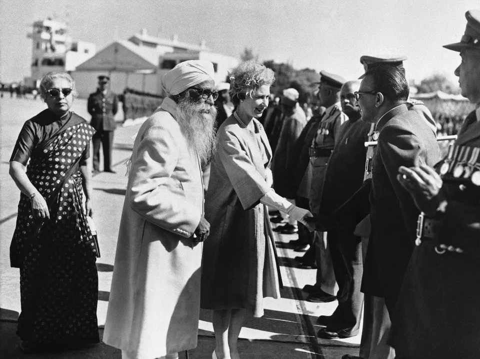 The Queen, accompanied by Gov. Gurmukh Nihal Singh, wearing a turban and a beard, shakes hands with a line of dignitaries and military officials.