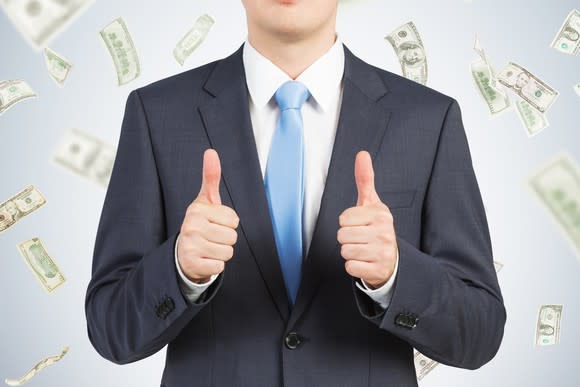 A person in a suit giving thumbs up as dollar bills fall in the background.