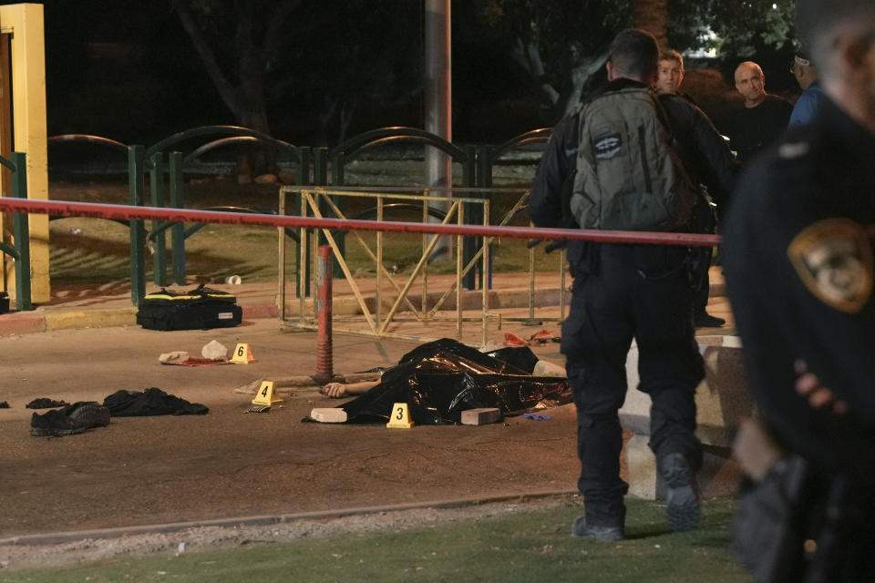 Israeli police officers stand next to the body of Palestinian attacker at the scene of a shooting attack outside the Israeli settlement of Maale Adumim, in the West Bank, Wednesday, Oct. 19, 2022. A Palestinian gunman who killed an Israeli soldier earlier this month was killed Wednesday after opening fire at a security guard at a West Bank settlement near Jerusalem. Israel Prime Minister Yair Lapid said Wednesday that Uday Tamimi, a Palestinian man from the Shuafat refugee camp near Jerusalem who was the subject of a more than weeklong manhunt by security forces, was killed by Israeli security forces. Police said he opened fire at a security guard, wounding him lightly. (AP Photo/Mahmoud Illean)