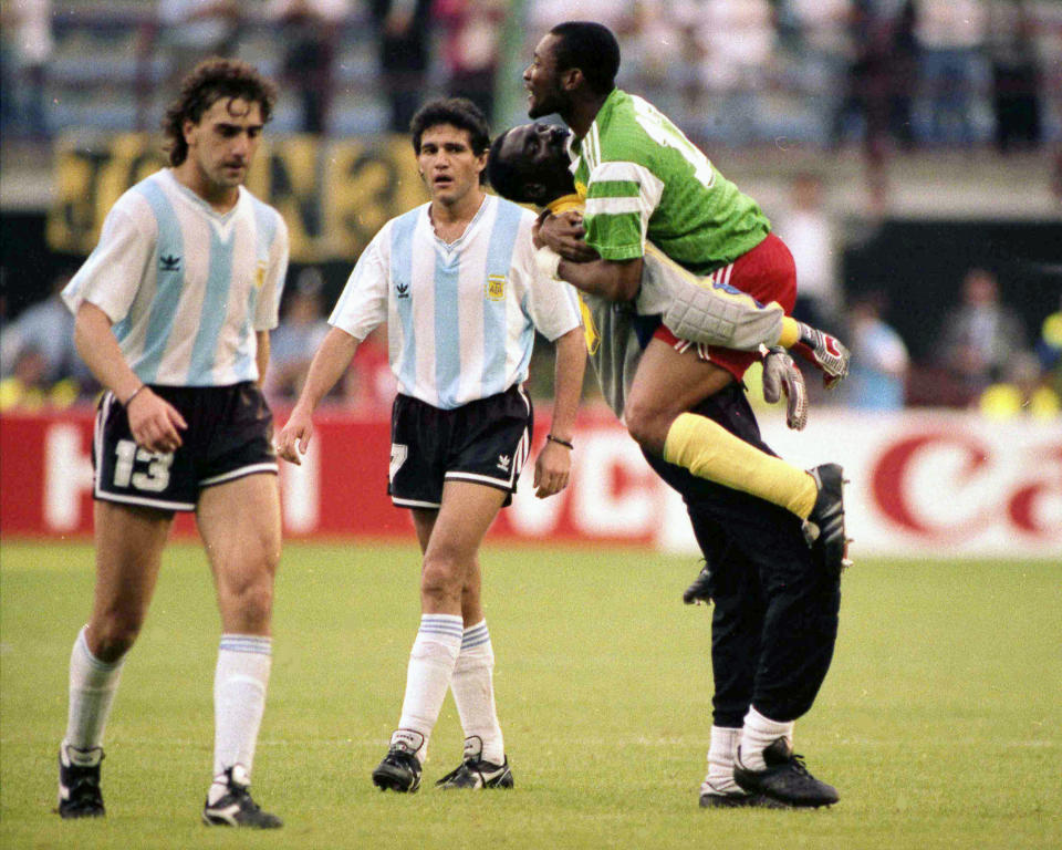 FILE - Dejected Argentine players Nestor Gabriel Lorenzo, left, and Jorge Luis Burruchaga walk off the pitch, past unidentified celebrating Cameroon players, after the opening match of the soccer World Cup, in Milan, Italy on June 8, 1990. The World Cup has produced its fair share of shocks, not least when Cameroon defeated defending champion Argentina 1-0 in 1990. (AP Photo/File)