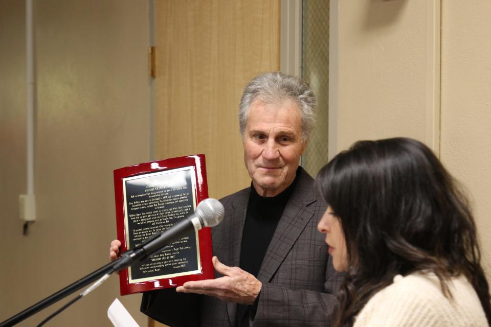Gary Niblett holds a plaque inducting him into the Carlsbad Hall of Fame on Jan. 28, 2023. City of Carlsbad Municipal Services Director Angie Barrios-Testa reads a proclamation issued by Mayor Dale Janway.