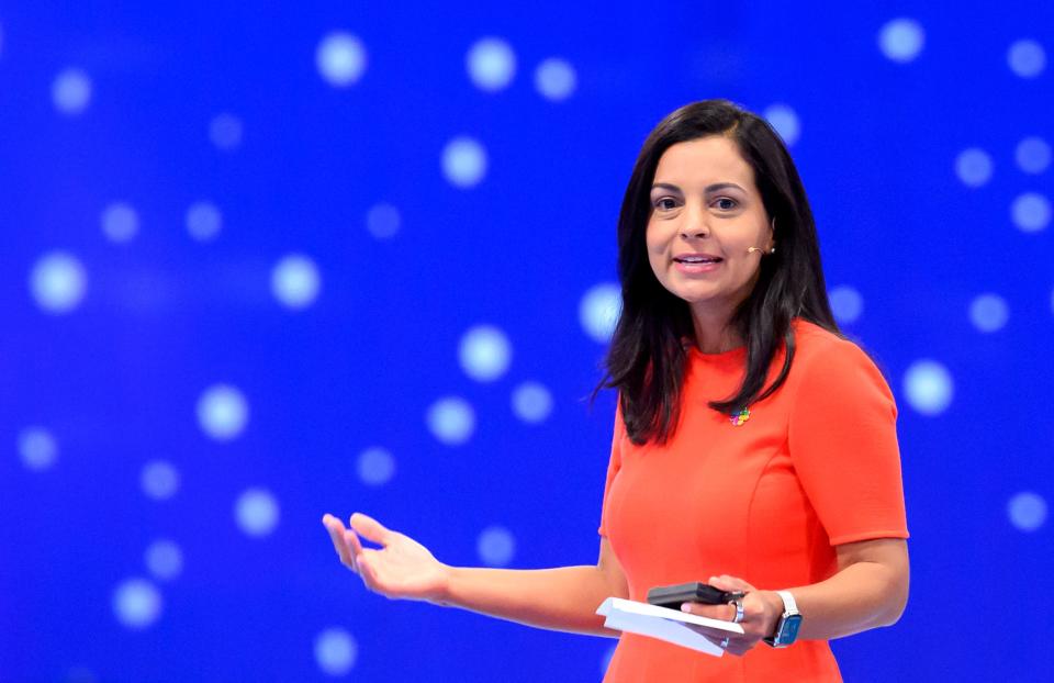 Lidiane Jones, former Slack CEO, speaks in front of a blue background while wearing an orange dress.