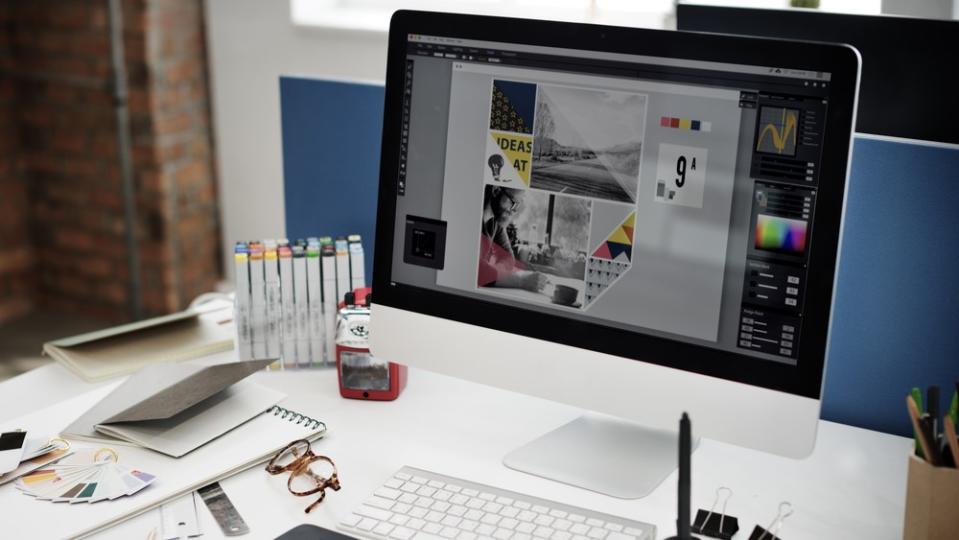 A desk with a computer showing graphic design tools.