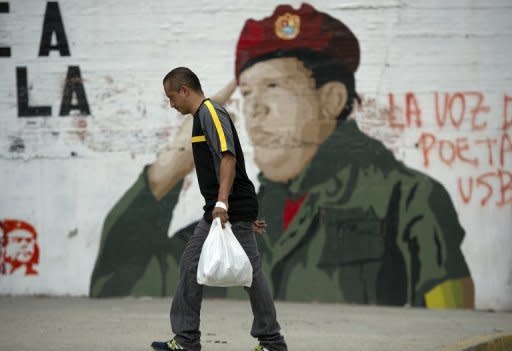 Un hombre camina frente a un mural con la imagen del presidente Chávez.