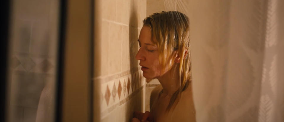 Cate Blanchett as Jasmine stands in a shower with water running, looking down with a solemn expression.