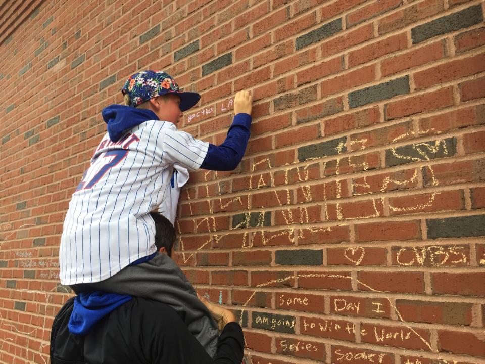 A young Cubs fan writes on the Wrigley brick wall. (Mike Oz / Yahoo Sports)