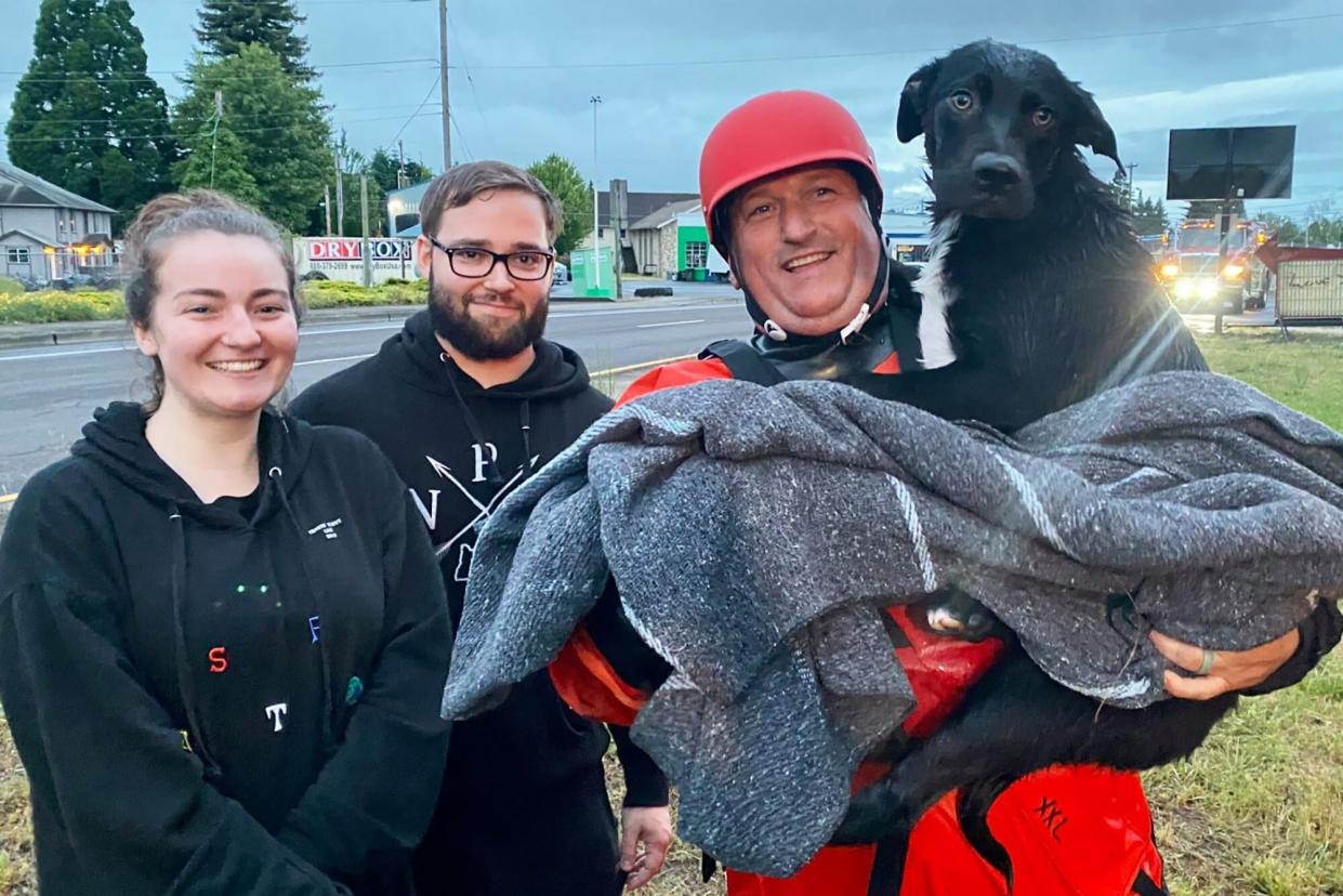 fireman holding black dog he rescue, standing with the couple that discovered the dog
