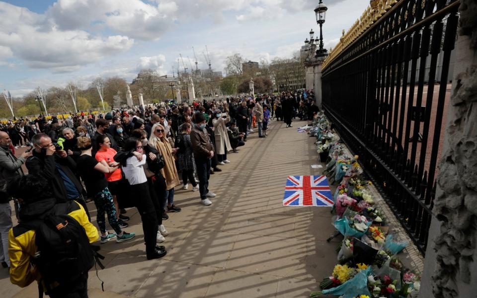 People view flowers left in front of the gate at Buckingham Palace in London - Matt Dunham/AP