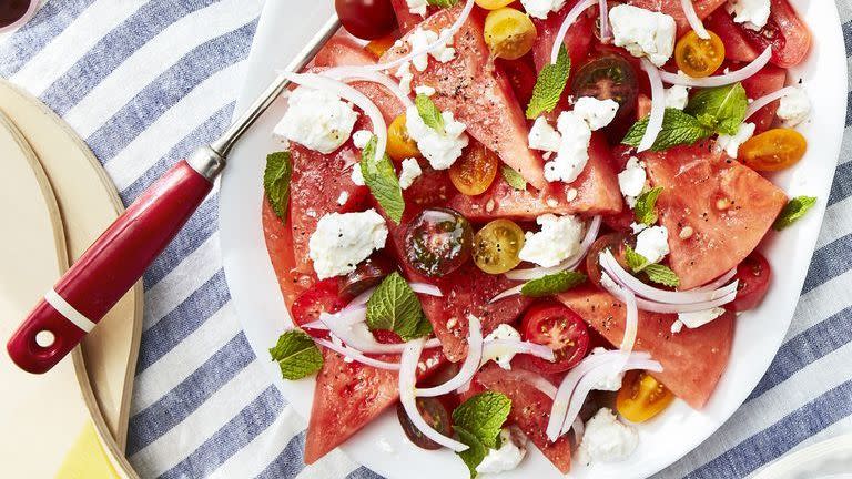 watermelon tomato feta salad on a white oval serving plate on a blanket on the beach