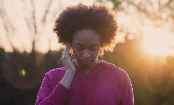 A woman listening on headphones outdoors at sunrise.