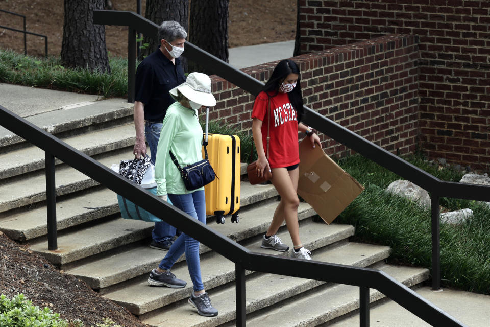 Charles Jacocks, rear, along with his wife Carrie and incoming freshman Ann Grace, right, carry their belongings as college students begin moving in for the fall semester at N.C. State University in Raleigh, N.C., Friday, July 31, 2020. The first wave of college students returning to their dorms aren’t finding the typical mobs of students and parents. At N.C. State, the return of students was staggered over 10 days and students were greeted Friday by socially distant volunteers donning masks and face shields. (AP Photo/Gerry Broome)