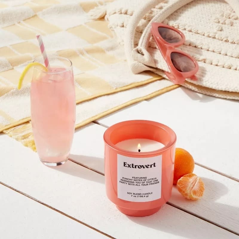 A lit "Extrovert" candle in a peach-colored glass jar