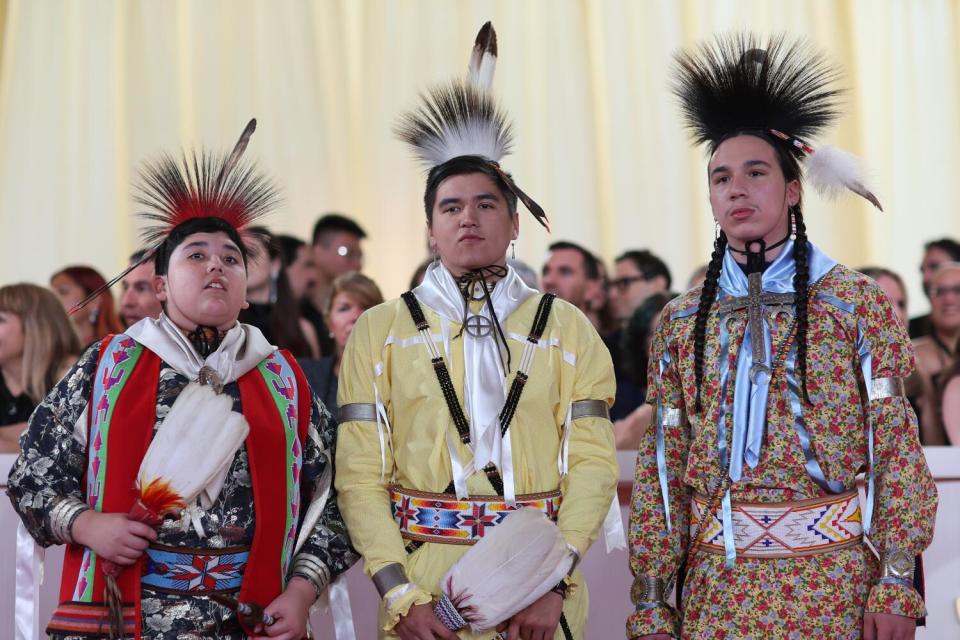 Three Osage Nation members wear traditional cloaks.