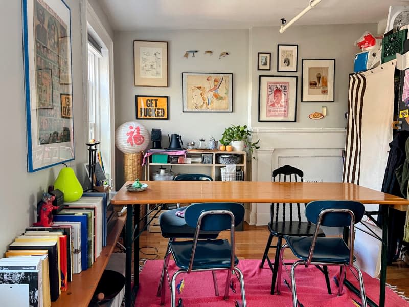 Large wooden table with four dark blue chairs across from a gallery wall of framed art.