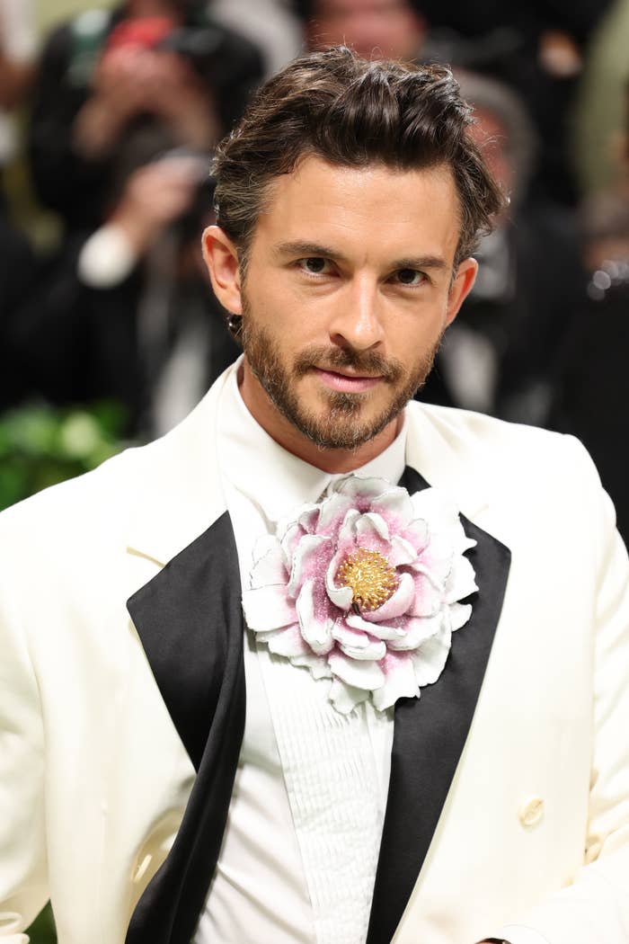 Jonathan Bailey dressed in a white suit with a large flower brooch on the lapel at a formal event