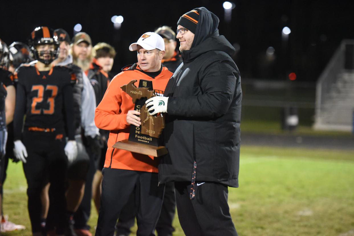 Almont coach James Leusby (left) accepts a regional championship trophy from Almont athletic director Ross Gauthier after a Division 6 regional final against Detroit Edison on Nov. 10.